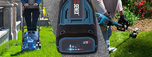 Person using a Senix X5 battery-powered lawn mower and trimmer on green grass near a flower bed