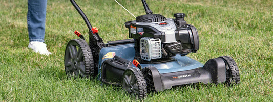 Gas-powered Senix lawn mower cutting grass on a sunny day with person in jeans and white shoes